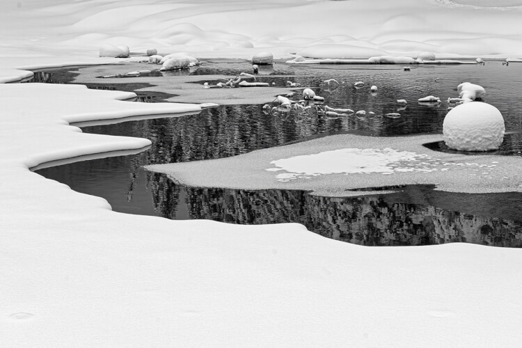 Snow along open water on a lake creates abstract patterns.